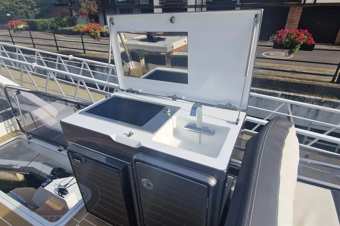 Boat's outdoor kitchenette with grill, sink, and mirror; features a black cabinet and sleek design on the deck.